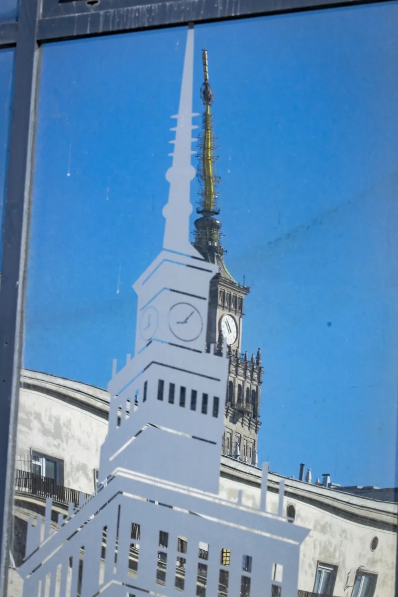 White outline of the Palace of Culture and Science on blue glass with the real spire behind